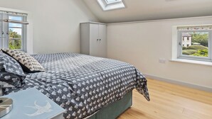 A bedroom with a bed, a wardrobe, and a desk with a lamp. There are skylights and a window providing natural light. - Rogeston House is a stunning and unusual annexe added to the original house. (Johnston, near Haverfordwest)