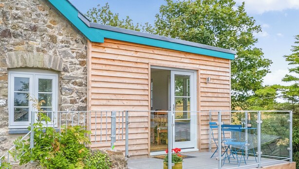 A wooden cabin with a balcony, stone walls, and a glass door leading to an interior space. - Rogeston House is a stunning and unusual annexe added to the original house. (Johnston, near Haverfordwest)