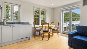 A modern kitchen with wooden cabinets, a dining table, and chairs. There is a blue sofa in the living area. - Rogeston House is a stunning and unusual annexe added to the original house. (Johnston, near Haverfordwest)