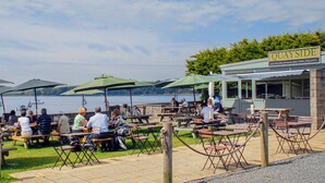 An outdoor dining area with tables and chairs, a sign reading "Quayside," and a view of the water and hills in the background. - 2 bedroom accommodation in Landshipping, near Narberth (Landshipping, near Narberth)