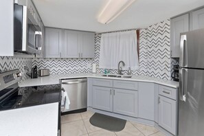 A modern kitchen with grey cabinets, a stainless steel dishwasher, and a built-in oven.