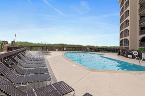 Un espace piscine avec des chaises longues et un bâtiment en arrière-plan.