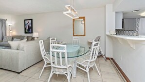 A modern living room with a glass dining table surrounded by white chairs, a grey sofa, and a white ceiling light fixture. - Waterfront *Extended Stay Discount* Pet Friendly (Myrtle Beach)
