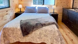 A cozy wooden cabin bedroom with a bed, two bedside lamps, a dresser, and a window with blinds. - Cozy Coastal Cabin #3 (Steuben)