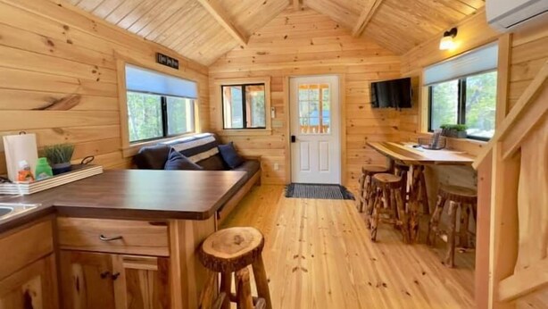 A cabin interior with a wooden interior, a kitchen area, and a seating area with a bench. - Cozy Coastal Cabin #3 (Steuben)