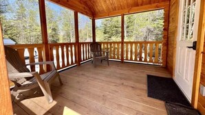 A wooden porch with a view of trees, a chair, and a door. - Cozy Coastal Cabin #3 (Steuben)