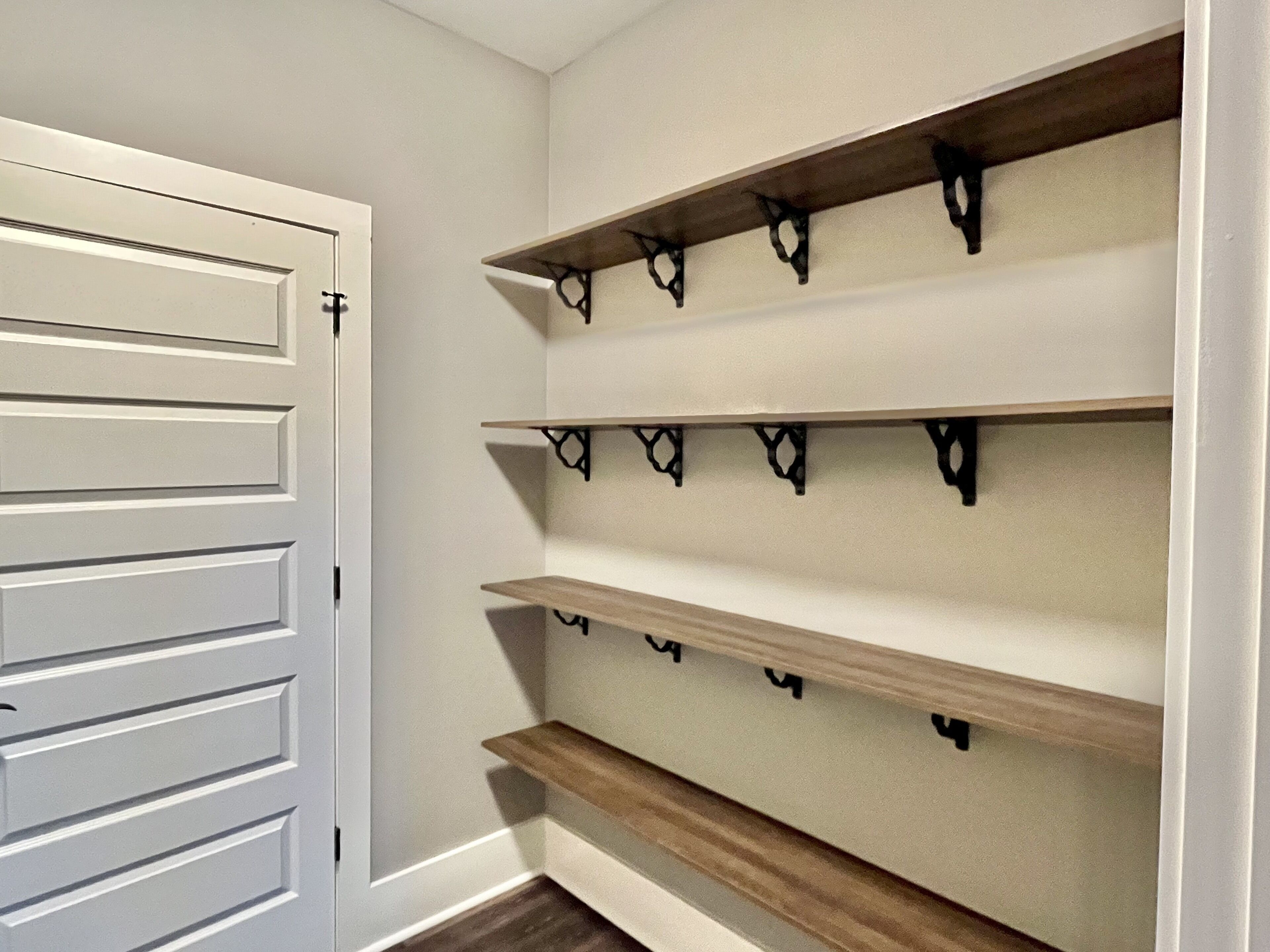 A hallway with white walls, a wooden door, and three wooden shelves with black metal brackets.