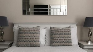 A neatly made bed with two patterned pillows, a large mirror above, and two bedside lamps on either side. - Number 46 (Hastings)