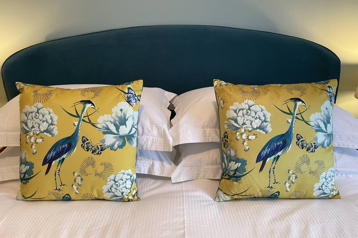 A bed with two pillows featuring a bird and floral design, a dark headboard, and white bedding.