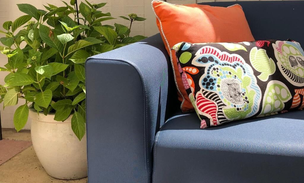 A blue sofa with a colorful pillow and a potted plant beside it.