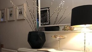 A room with a white cabinet, a black vase with branches, a mirror, and a lamp. - Number 46 (Hastings)
