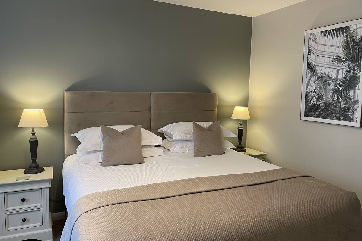 A neatly made bed with a headboard, two bedside lamps, a small bedside table, and a framed picture on the wall.