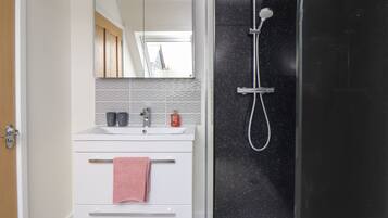 Une salle de bain avec un meuble-lavabo blanc, un miroir, un évier, une serviette et une douche dont le mur est noir et parsemé de petites taches.