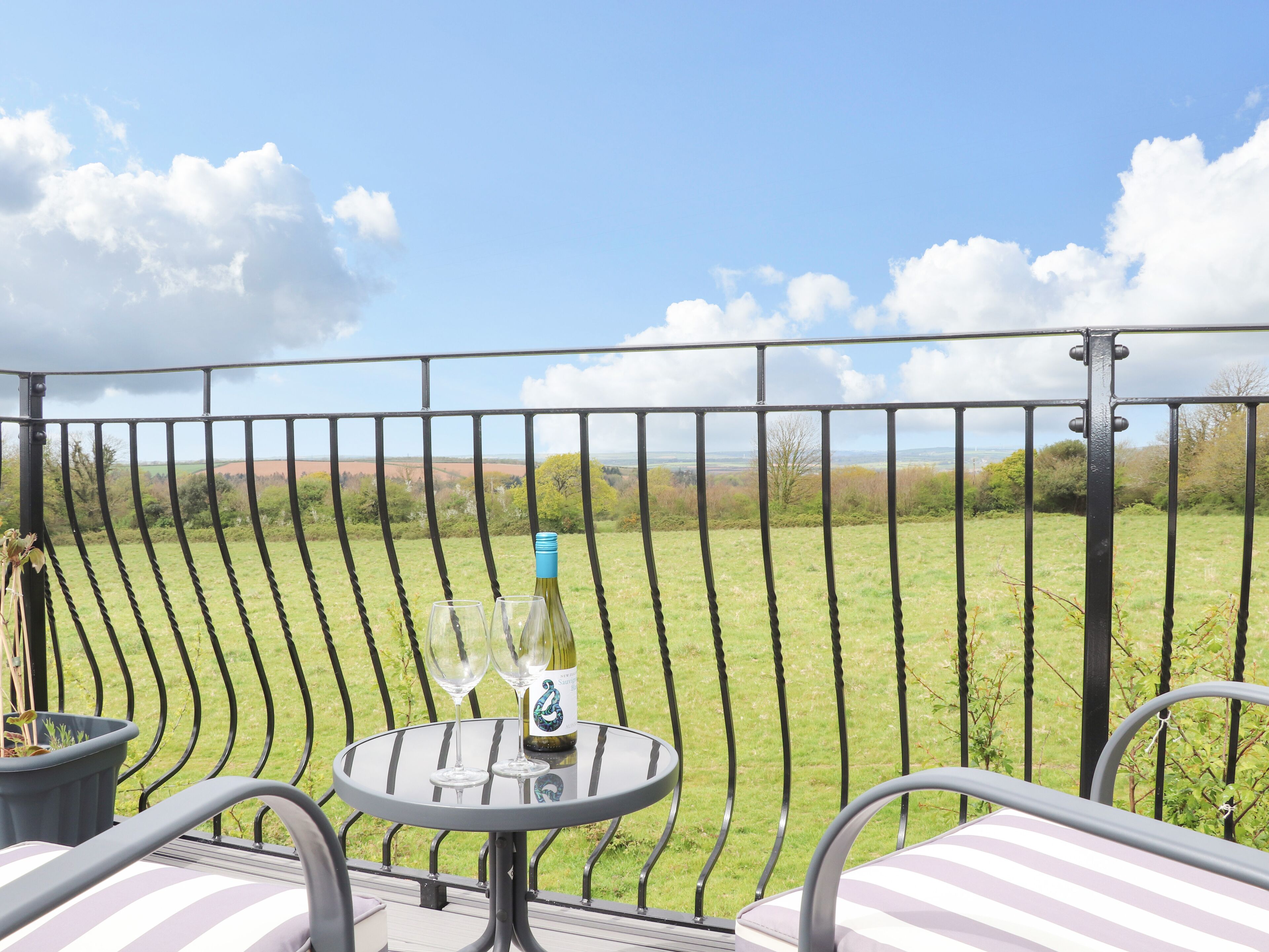 Un balcon avec une table, deux verres à vin et une bouteille de vin.