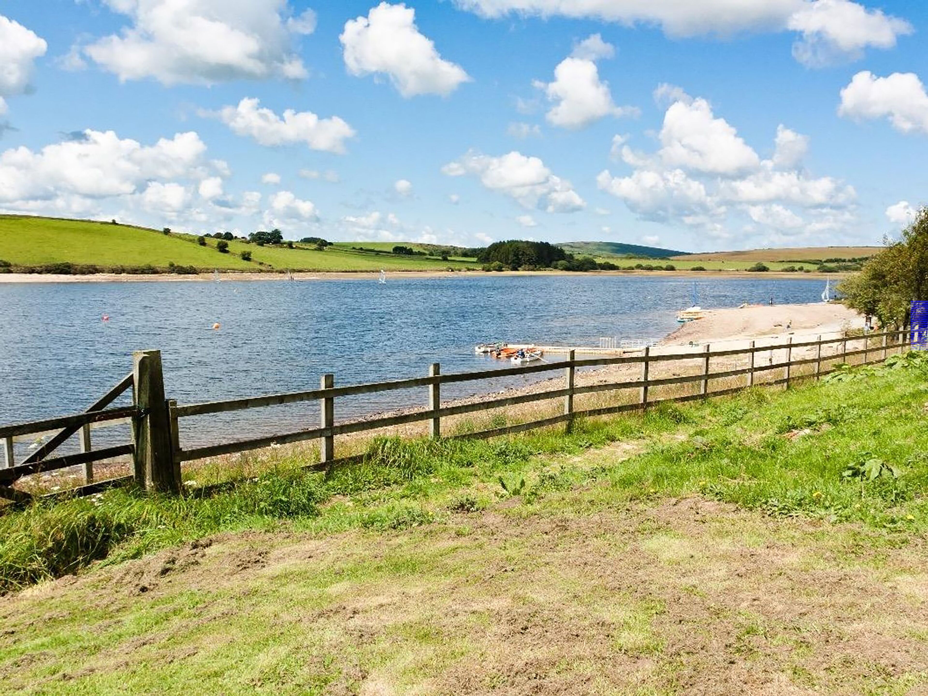 A riverside view with a wooden fence, grassy banks, and a sandy beach area.