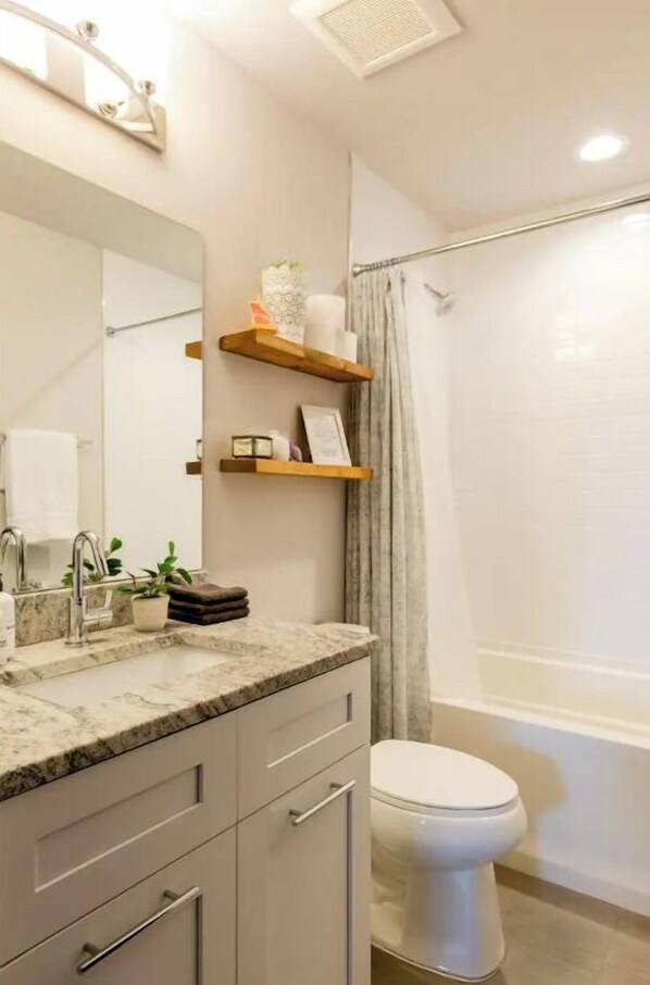 Un baño moderno con lavamanos de mármol, un espejo grande, repisas de madera, inodoro y zona de ducha.