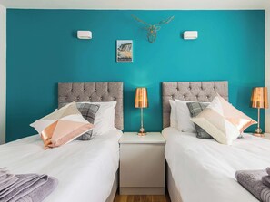 A twin bedroom with two beds, a nightstand, a lamp, a wall-mounted picture, and a decorative antler.