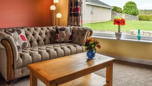 Ein Wohnzimmer mit einer Couch, einem Couchtisch aus Holz und einem Fenster mit Blick auf ein Haus und einen Garten.