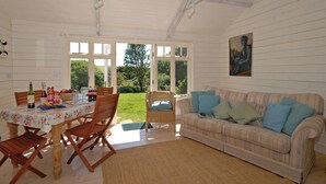 A room with a dining table set for two, a sofa with cushions, and a painting on the wall. - Manorbier Boat House (Manorbier)