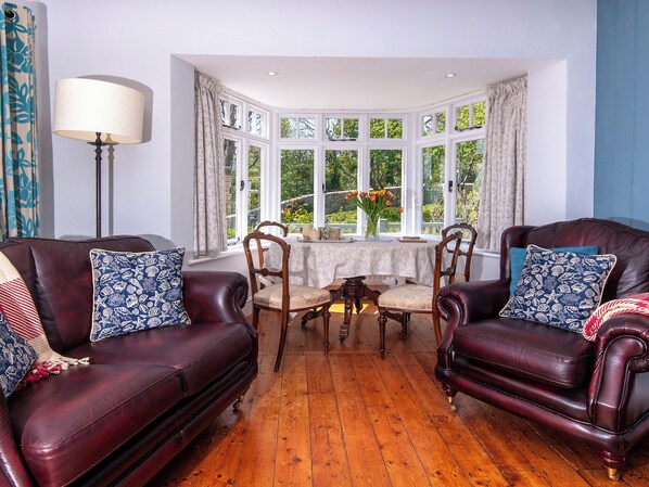 A room with two leather sofas, a wooden table, and a bay window with curtains. - Manorbier Boat House (Manorbier)