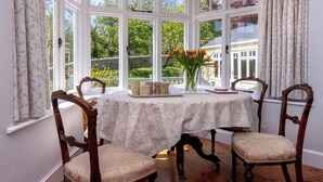 A room with a bay window, a table with chairs, and a vase with flowers. - Manorbier Boat House (Manorbier)