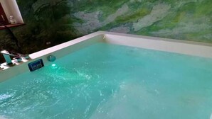 Una bañera de hidromasaje rectangular con agua cristalina, un panel de control y una pared verde al fondo.