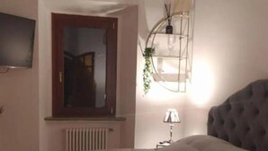 Un dormitorio con una cama grande, techo de madera, radiador, televisor en la pared y lámpara colgante.