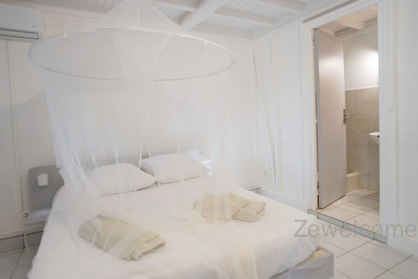 Un dormitorio con cama con dosel, una mesita de noche y un baño visible a través de una puerta abierta.