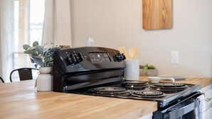 A kitchen with a black stove, wooden countertop, and a white vase with a plant.