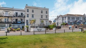 Una strada costiera con edifici, tra cui un caffè chiamato 'Babbacombe Bay Café' e un albergo chiamato 'Royal Hotel'.