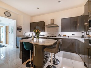 A modern kitchen with a marble island, dark cabinetry, and a stainless steel range hood. - 6 bedroom accommodation in Torquay (Torquay)