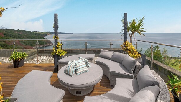 Una terrazza con un divano curvo e un tavolino rotondo, vista su uno specchio d'acqua.
