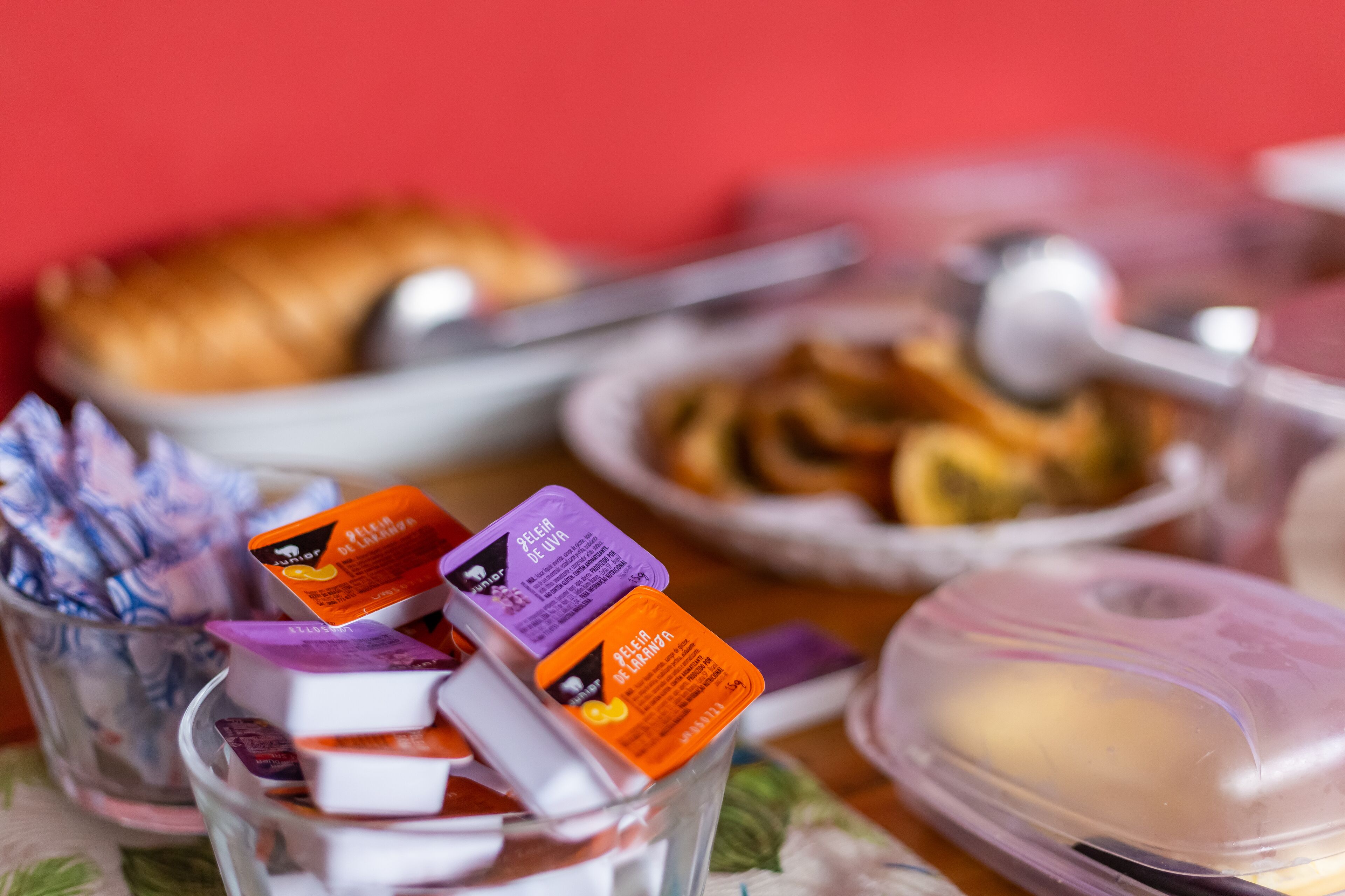 Un tavolo con diversi cibi e condimenti, tra cui un bicchiere con cibo confezionato, una ciotola di pasticcini e un contenitore con un cucchiaio.