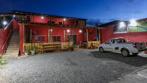 En rød bygning med grusvej, en hvid pick-up lastbil parkeret, og en trappe til indgangen.