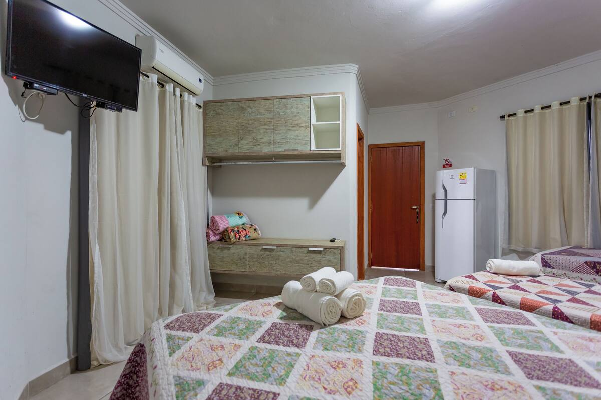 A hotel room with a bed, a television, a wardrobe, a desk, and a refrigerator.