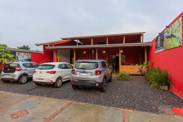 A building with a red exterior, a covered entrance, and three parked cars in front. - Pousada Salomé (Bonito)