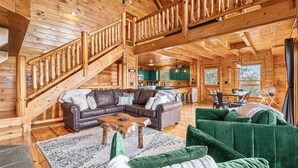 A spacious wooden cabin with a large living area featuring a sectional sofa, a coffee table, and a staircase with a wooden railing.