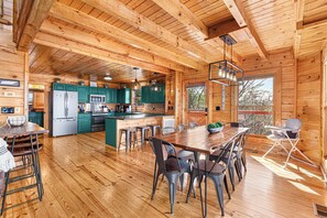 A spacious wooden cabin with a large dining area, kitchen, and a view of the outdoors.