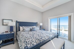 Een slaapkamer met een groot bed, twee nachtkastjes, een bankje en uitzicht op de oceaan door grote ramen.