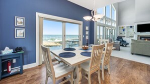 A dining area with a view of the beach, wooden chairs, a table with placemats, and a blue wall. - Exquisite Private Lake Front Family Home (Manistee)