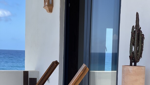 A wooden lounge chair with a woven basket and a small table, positioned on a balcony with a view of the ocean. - Casa Lúa in front of the sea (Guía)
