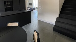A modern kitchen with dark cabinetry, a dining area with a round table and chairs, and a staircase leading to an upper floor. - Casa Lúa in front of the sea (Guía)