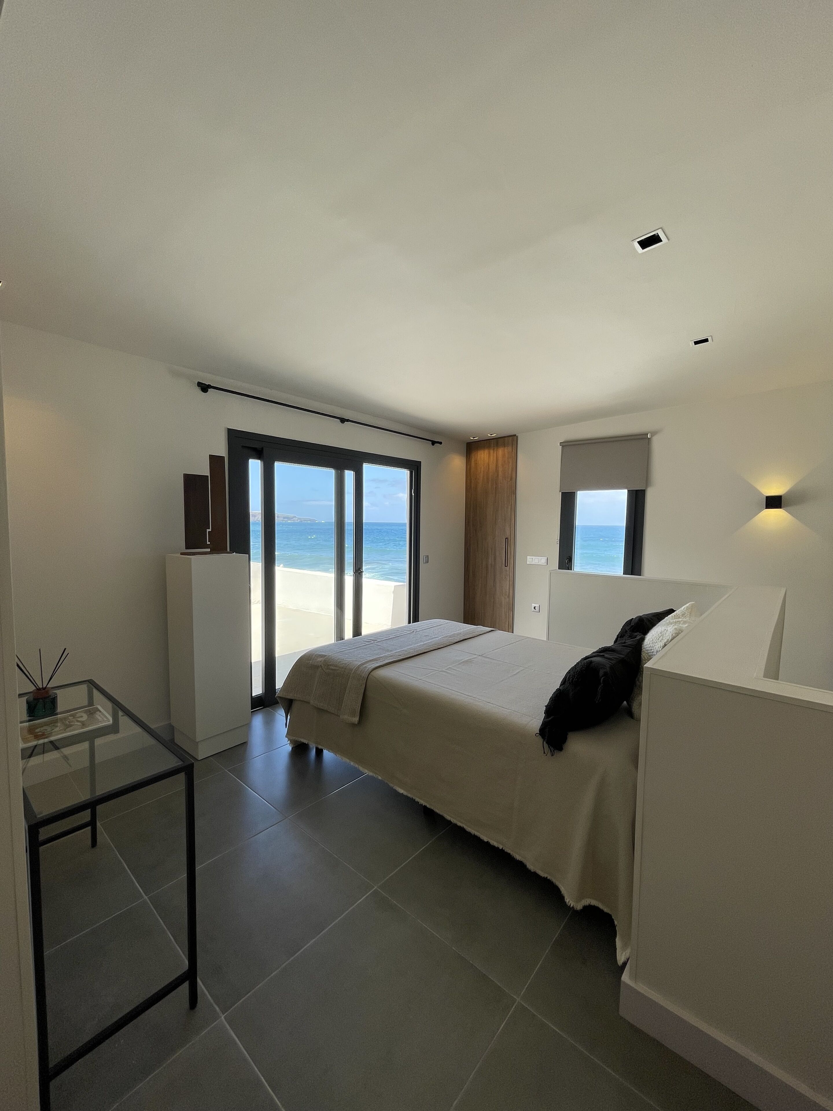 Une chambre à coucher moderne avec un lit, une table en verre, une armoire et une vue sur la mer.