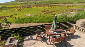 Eine Terrasse mit Holzmöbeln und einem Tisch, mit Blick auf eine grüne Landschaft mit Hügeln und einem Berg.