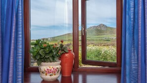 Ein Fenster mit Blick auf eine gebirgige Landschaft, ein Blumentopf und eine Vase auf einer Holzablage.