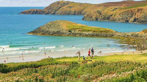 Eine Küstenlandschaft mit Felsen, einem Strand und Menschen bei verschiedenen Aktivitäten.