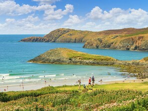 A coastal landscape with rocky outcrops, a beach, and people engaging in various activities. - 4 bedroom accommodation in St Davids, near Whitesands (St Davids, near Whitesands)
