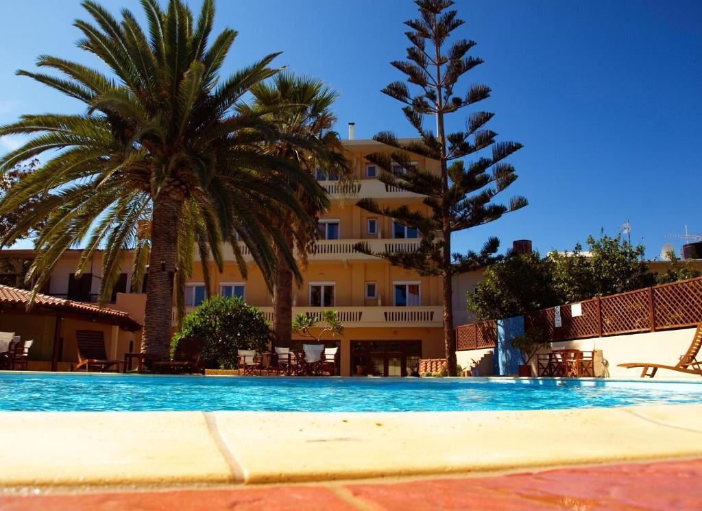 Ein Hotel mit Schwimmbad, Palmen und einem Gebäude mit Balkonen.