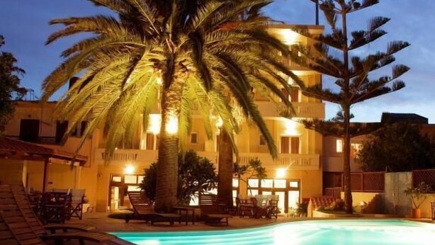 A poolside area with lounge chairs and a building with multiple floors and balconies. - Kissamos Hotel (Kissamos)