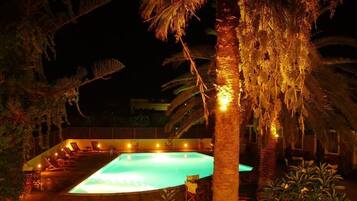 A nighttime view of a swimming pool area with lounge chairs and palm trees.